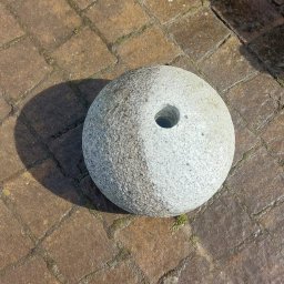 Angelika Liszka Rudy czyścik - Granitowa kula z otworem, częściowo oczyszczona, leżąca na brązowej kostce brukowej.