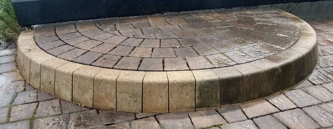 Półokrągłe schody z kostki brukowej, widoczne ślady wilgoci i niewielki mech w szczelinach.