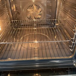 Sprzątanie z Pasją - Wnętrze czystego piekarnika z metalową kratką i wentylatorem na tylnej ściance. Oświetlenie wewnątrz piekarnika podkreśla jego czystość.