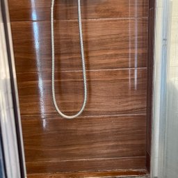 Sprzątanie z Pasją - Błyszcząca, brązowa ściana kabiny prysznicowej z widoczną słuchawką i wężem prysznicowym. Widoczne ślady po wodzie na panelach.