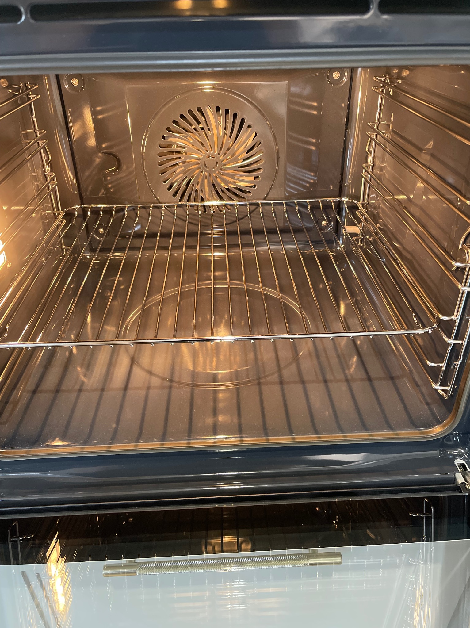 Wnętrze czystego piekarnika z metalową kratką i wentylatorem na tylnej ściance. Oświetlenie wewnątrz piekarnika podkreśla jego czystość.