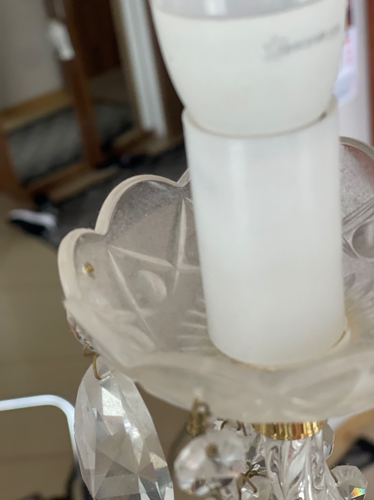 Kryształowy żyrandol z bliska, z widoczną żarówką i dekoracyjnymi elementami, sugerujący delikatne oświetlenie wnętrza.