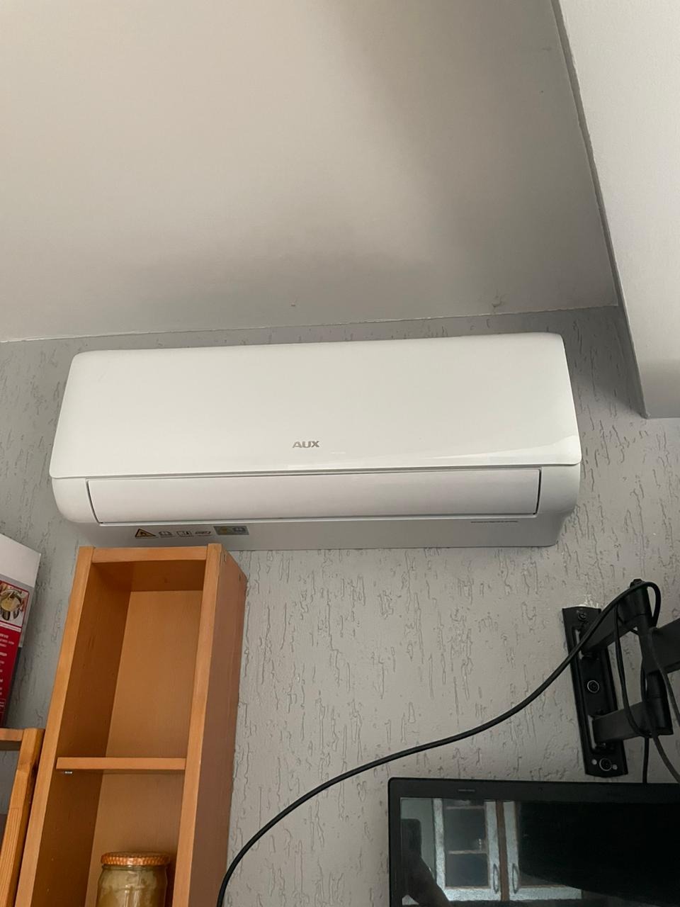 Zamontowana jednostka klimatyzacji AUX w mieszkaniu we Wrocławiu, widoczna na tle ściany o szarej strukturze, obok półki i uchwytu do telewizora.