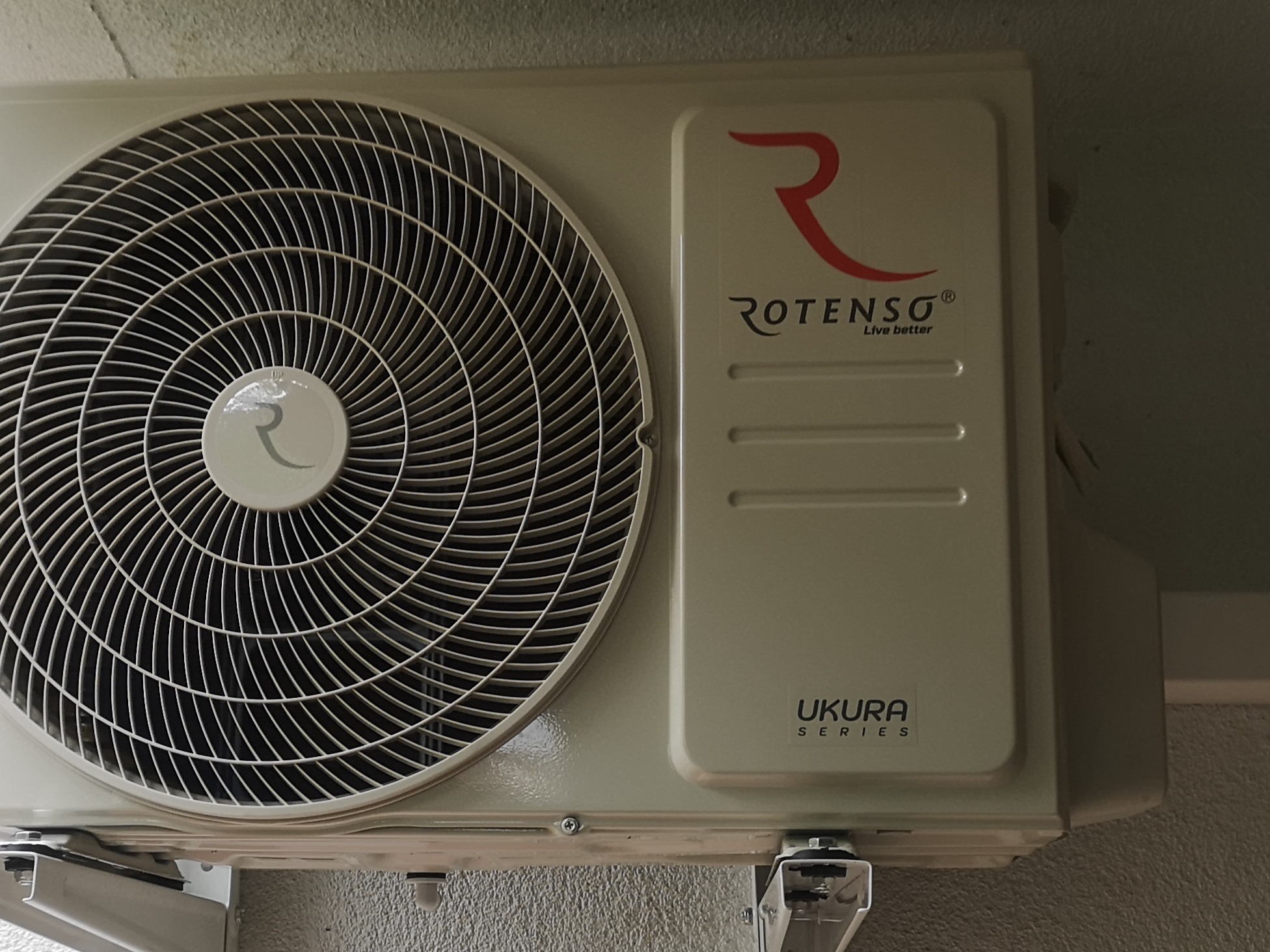 Kremowy klimatyzator Rotenso Ukura Series zamontowany na ścianie, widoczny wentylator i logo producenta.