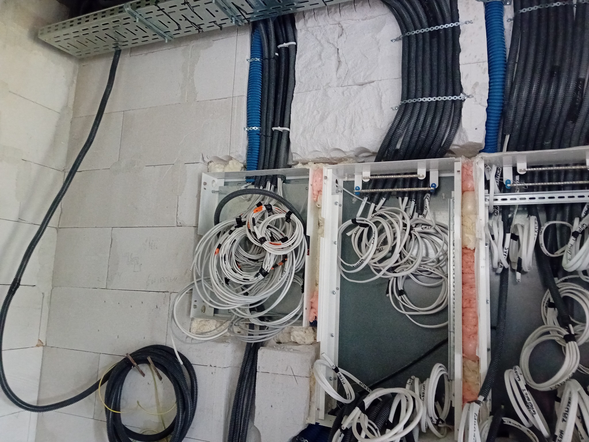 Rozdzielnia elektryczna w trakcie montażu, widoczne kable w peszlach i skrzynkach, ściany z betonu komórkowego.
