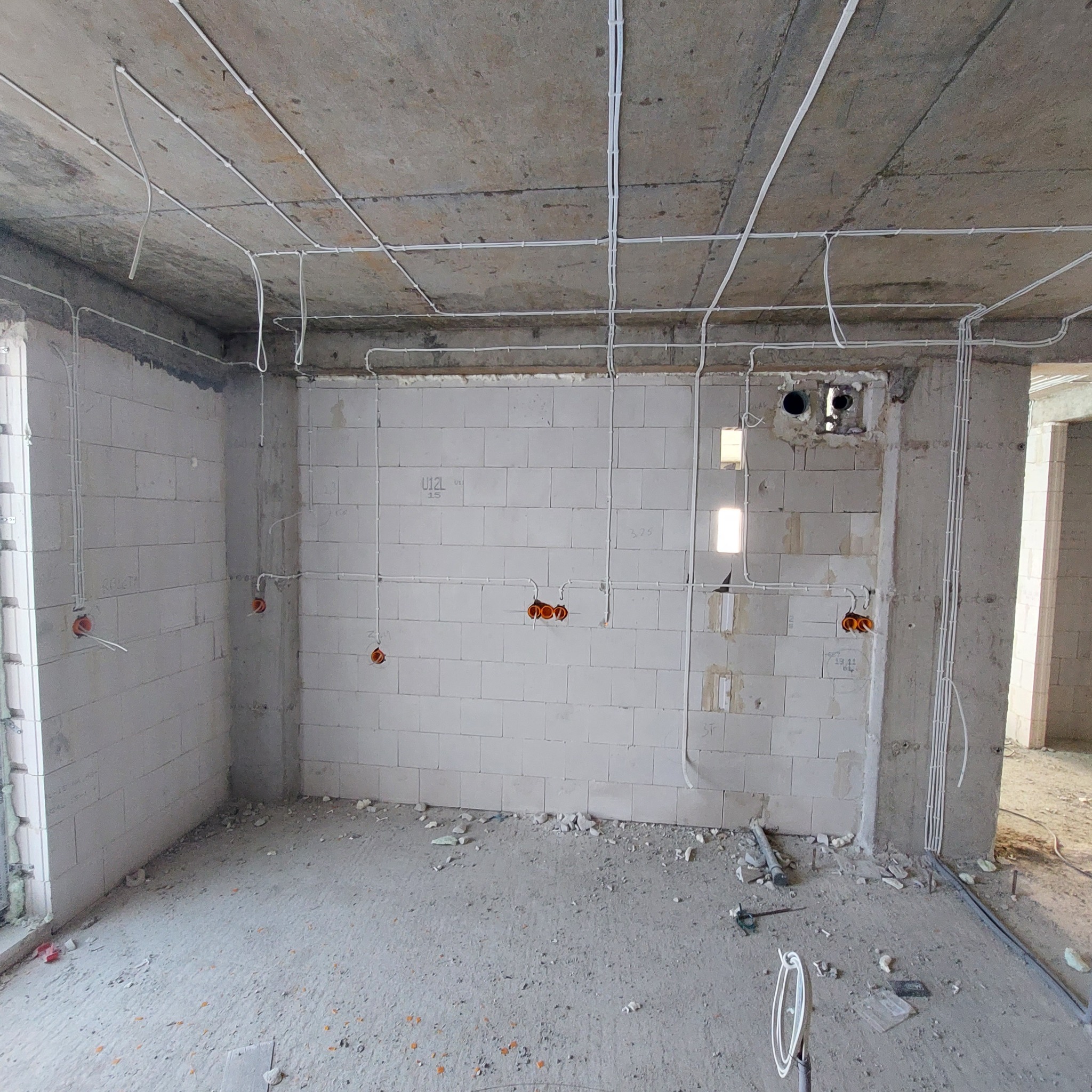 Surowy stan wnętrza w trakcie prac elektrycznych: widoczne kable prowadzone po suficie i ścianach, puszki instalacyjne w ścianach z betonu komórkowego, narzędzia na podłodze.