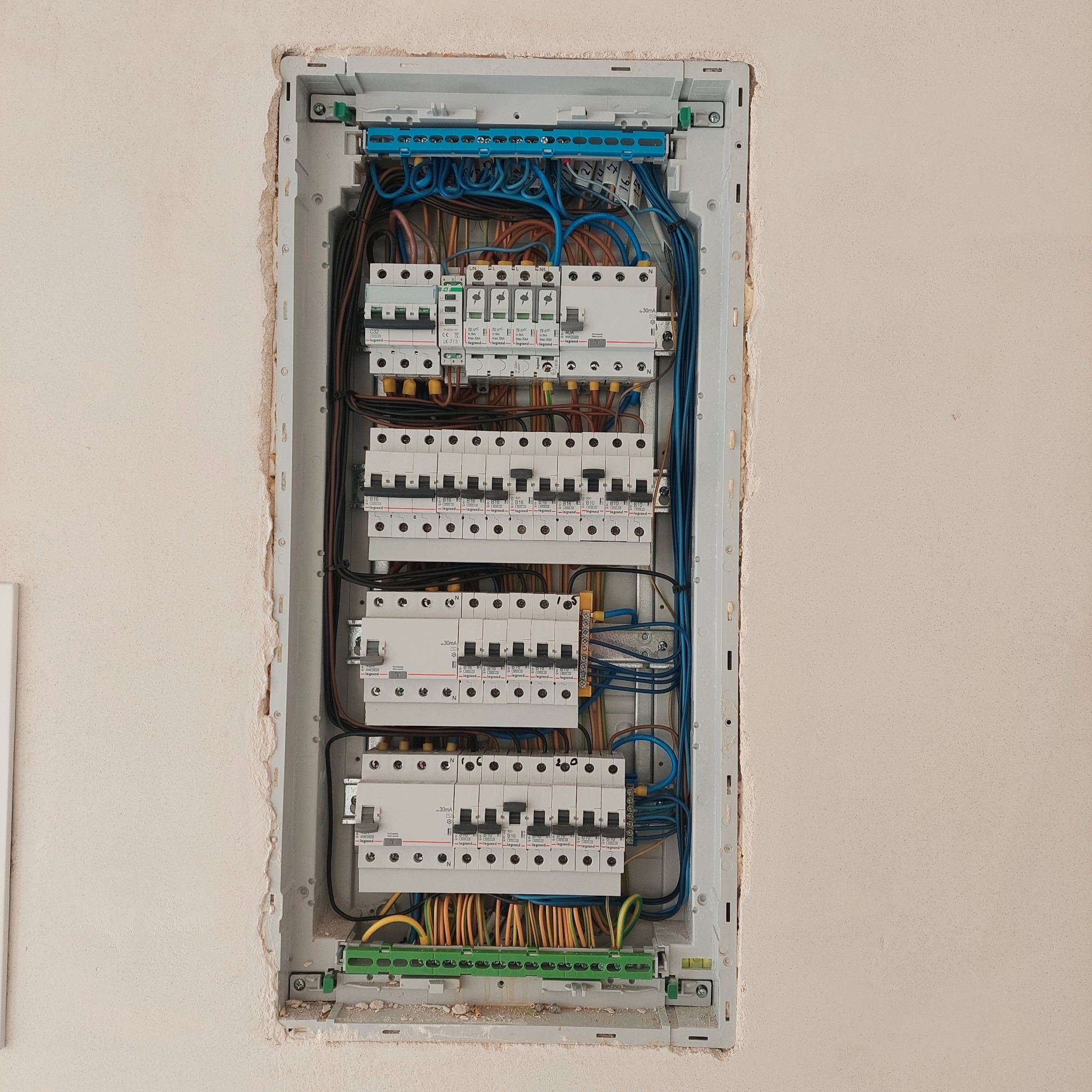 Otwarta skrzynka rozdzielcza z zainstalowanymi bezpiecznikami i okablowaniem w ścianie podczas prac w Żyrardowie, widoczne detale połączeń i oznaczenia na urządzeniach.