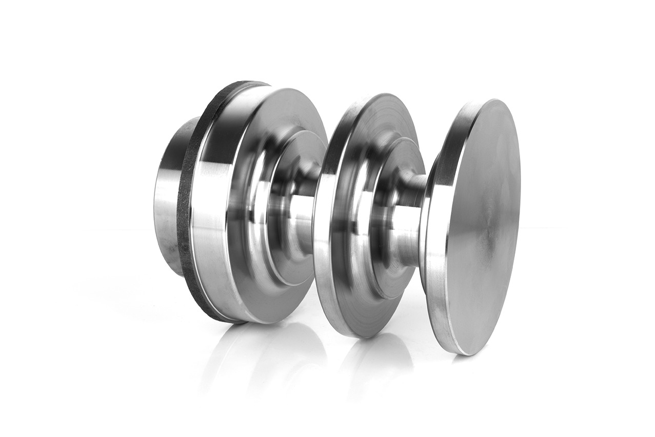 Precyzyjnie obrobiony, symetryczny element metalowy o gładkiej, srebrzystej powierzchni, składający się z trzech dysków o różnych średnicach połączonych wąskim trzpieniem, ustawiony na białym tle.
