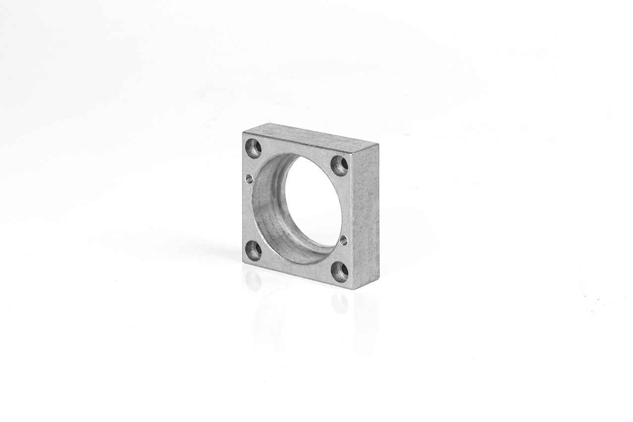 Szlifowany, aluminiowy, kwadratowy element z otworem centralnym i czterema otworami na śruby w rogach, leżący na białym tle.