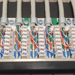 Baker Networks Tadeusz Piekarski - Zakończone kable sieciowe w panelu krosowym, z precyzyjnie ułożonymi kolorowymi żyłami. Widoczne metalowe uchwyty mocujące kable. Estetyczne i profesjonalne wykonanie.