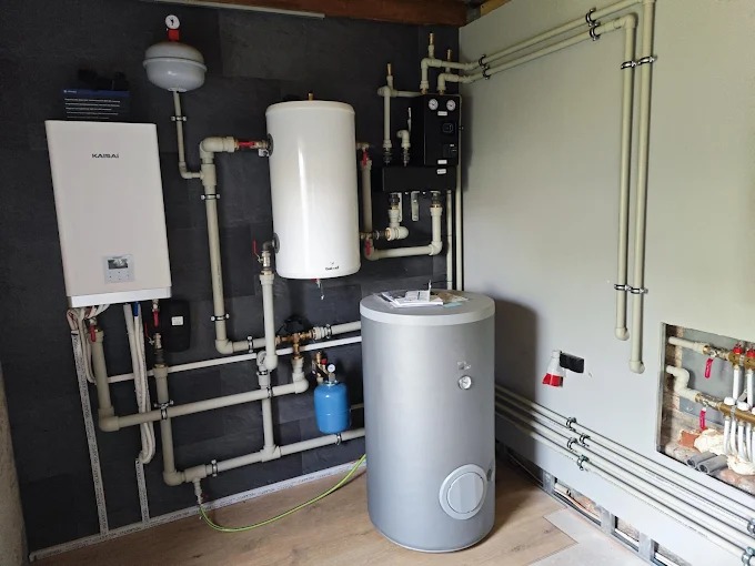 Kompletna instalacja grzewcza z kotłem Kaisai, zbiornikami i rozdzielaczami, rury prowadzone wzdłuż ścian. Nowoczesny system grzewczy w kotłowni.