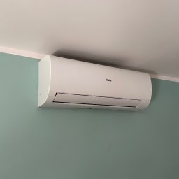 GREENFLOW SOLUTIONS SPÓŁKA Z OGRANICZONĄ ODPOWIEDZIALNOŚCIĄ - Biała klimatyzacja Haier zamontowana na zielonej ścianie w Bełku, widok z dołu.