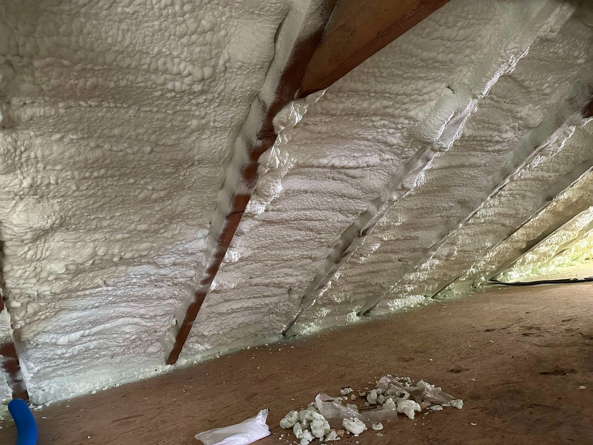 Poddasze ocieplone pianką poliuretanową, widoczne krokwie i resztki pianki na podłodze po aplikacji, z workiem foliowym w rogu