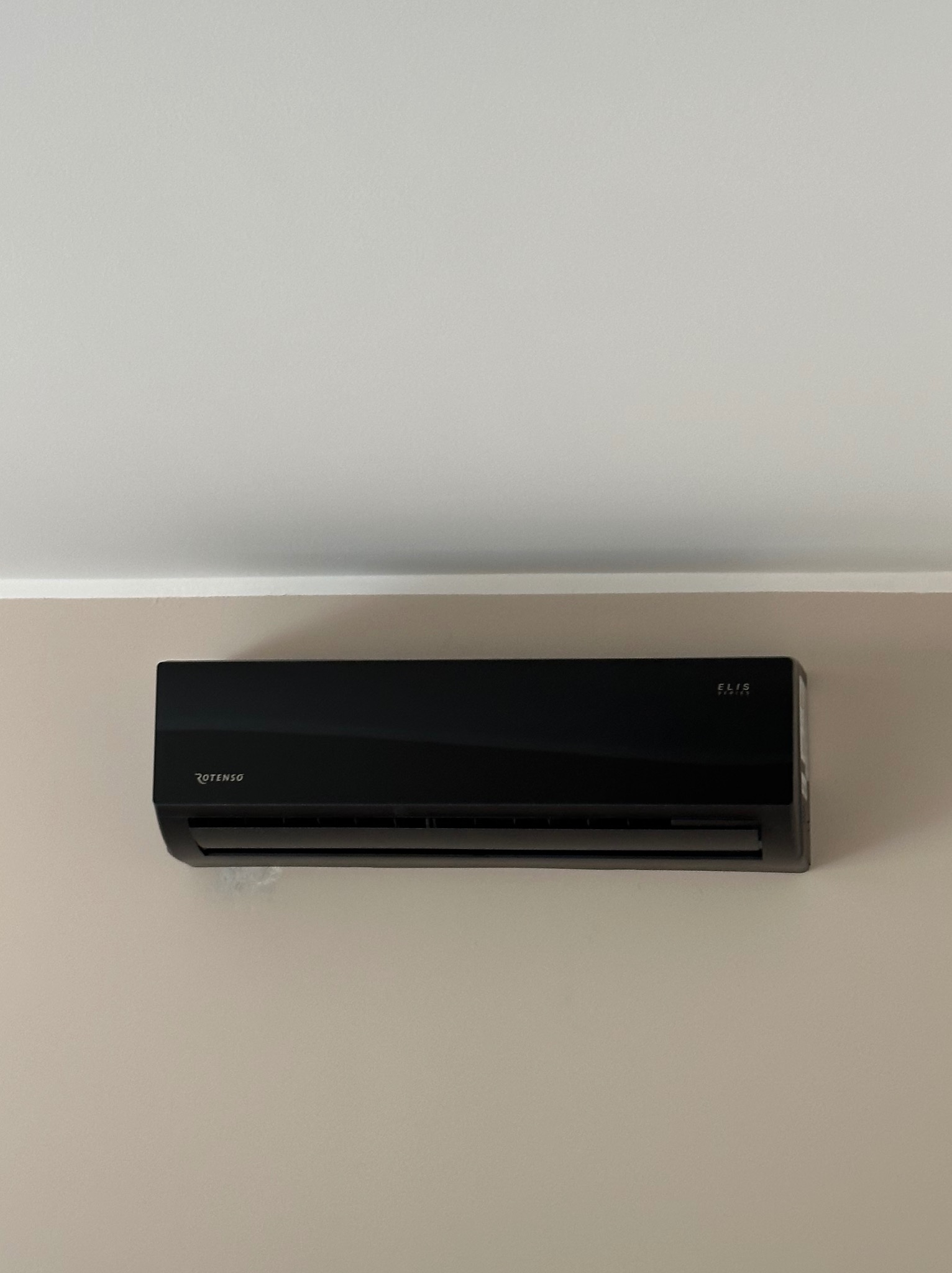 Czarny klimatyzator Rotenso Elis Series zamontowany na jasnej ścianie pod sufitem, widoczne logo producenta.