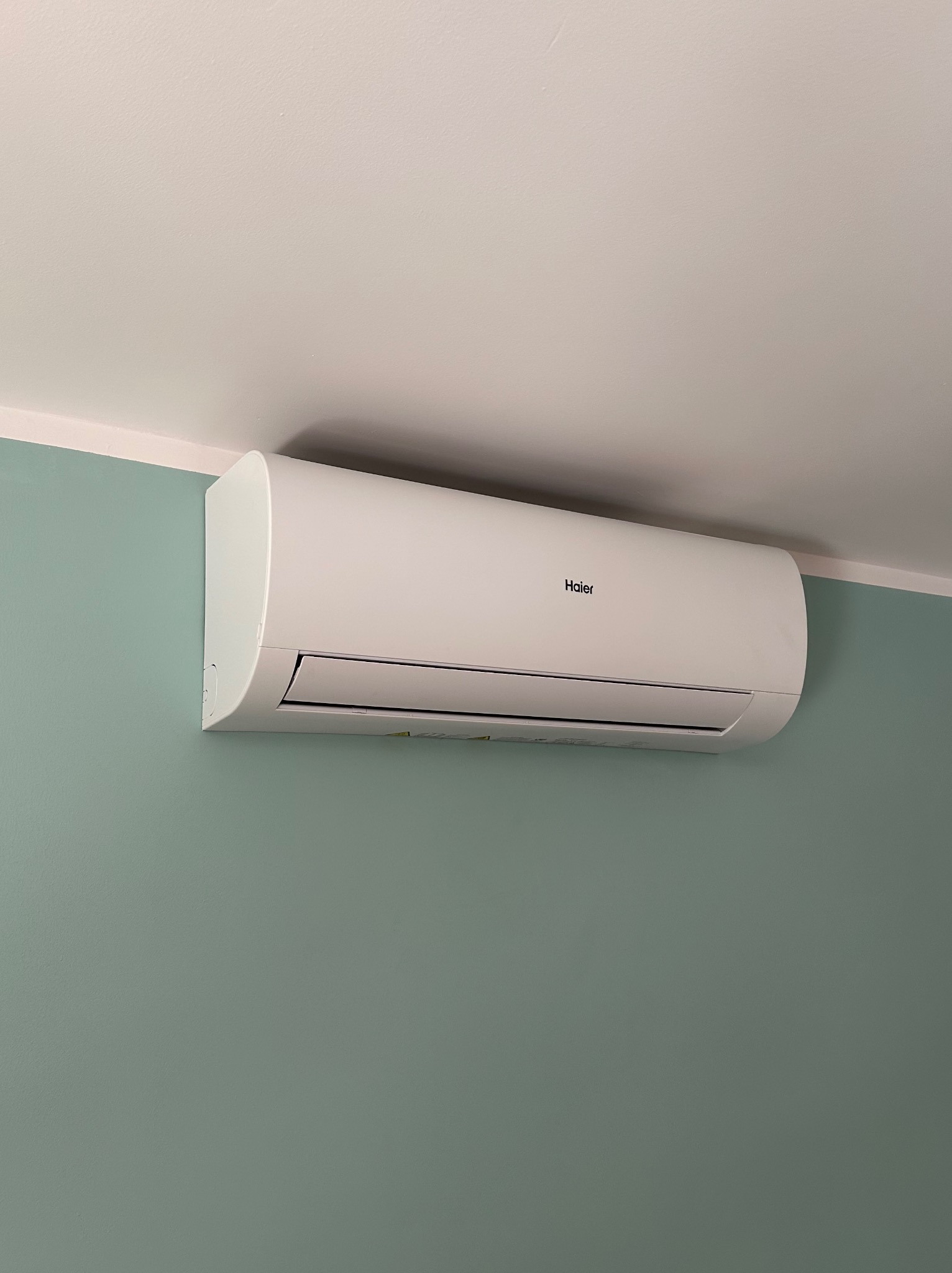 Biała klimatyzacja Haier zamontowana na zielonej ścianie w Bełku, widok z dołu.