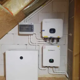 Kompletny system fotowoltaiczny Growatt z magazynem energii, zamontowany w pomieszczeniu z surowymi ścianami z bloczków i drewnianą podłogą.