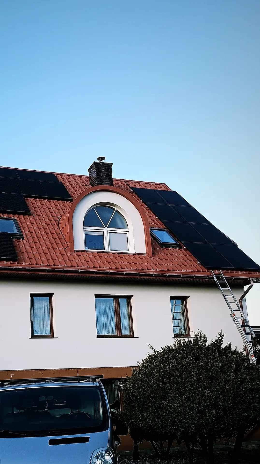 Instalacja paneli fotowoltaicznych na dachu domu jednorodzinnego w Łomży z użyciem drabiny, widoczny samochód dostawczy firmy u dołu kadru.