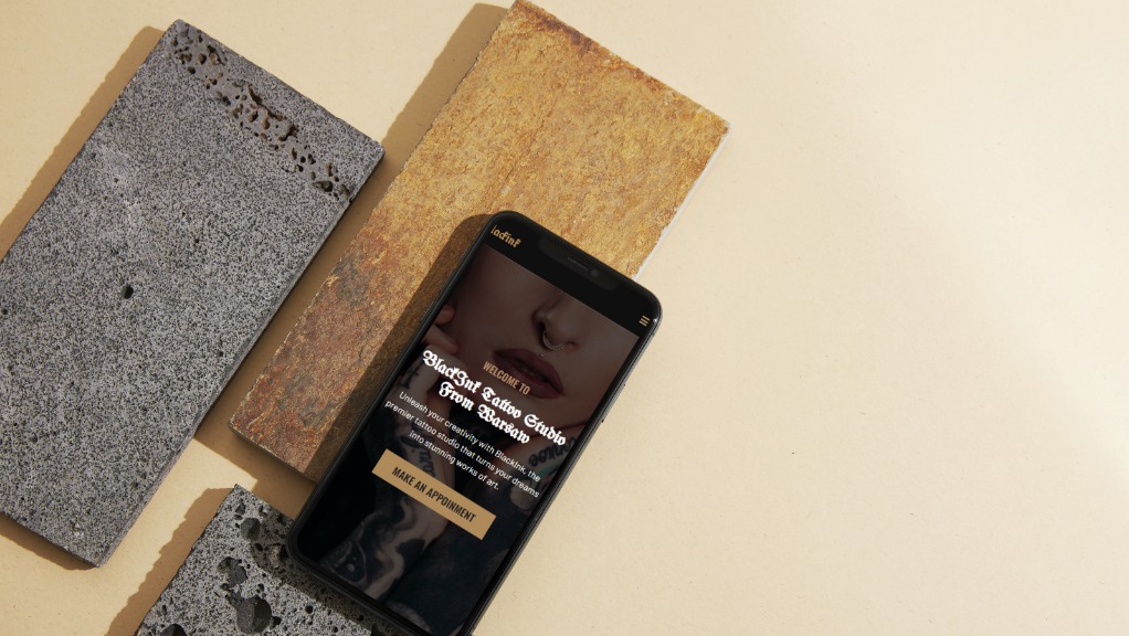 Smartfon wyświetlający stronę internetową studia tatuażu BlackInk z Warszawy, otoczony dekoracyjnymi płytkami z szarego i żółtego kamienia na beżowym tle.