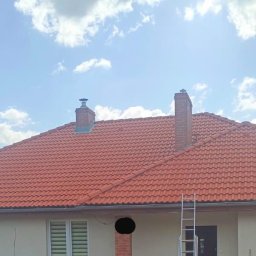 Marcel Rosiński - Czerwona dachówka na domu jednorodzinnym, widoczna drabina oparta o ścianę, błękitne niebo z chmurami w tle.