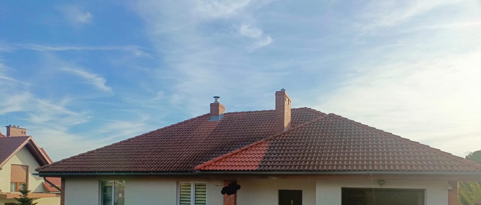 Czerwona dachówka na dwuspadowym dachu domu jednorodzinnego z ceglanymi kominami na tle błękitnego nieba z delikatnymi chmurami.