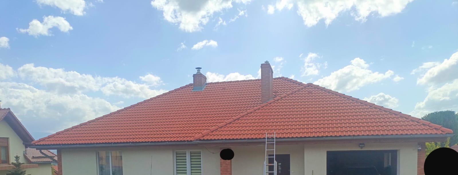 Czerwona dachówka na domu jednorodzinnym, widoczna drabina oparta o ścianę, błękitne niebo z chmurami w tle.