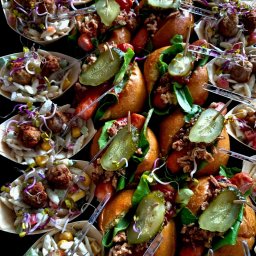 Catering & Cooking Corner - Widok z góry na aranżację finger food: miniaturowe hot dogi z sałatą, ogórkiem konserwowym i prażoną cebulką oraz sałatki makaronowe z pulpetami, podane w łódeczkach z jasnego drewna...