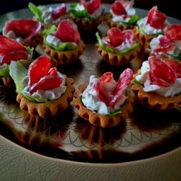 Catering & Cooking Corner - Talerz z tartaletkami: kruche babeczki wypełnione białym kremem, zieloną sałatą i plasterkami czerwonego salami, ułożone na złotej, dekoracyjnej tacy.