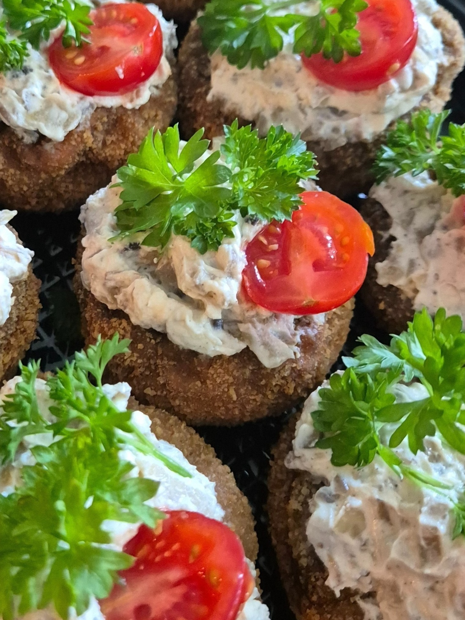 Zbliżenie na kanapki z pastą, pomidorem i natką pietruszki, ułożone na czarnej tacy.