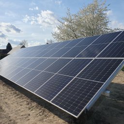 Tompor - Panel słoneczny na metalowej konstrukcji, z kwitnącym drzewem i błękitnym niebem w tle, na przygotowanym podłożu.