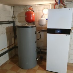 Tompor - Biała pompa ciepła Viessmann obok szarego zbiornika akumulacyjnego w kotłowni wyłożonej kafelkami, widoczne rury instalacyjne.