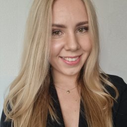 Kancelaria Księgowa Dorota Lotko - Uśmiechnięta blondynka w czarnej marynarce i delikatnym złotym naszyjniku z zawieszką w kształcie serca, portret na jasnym tle.