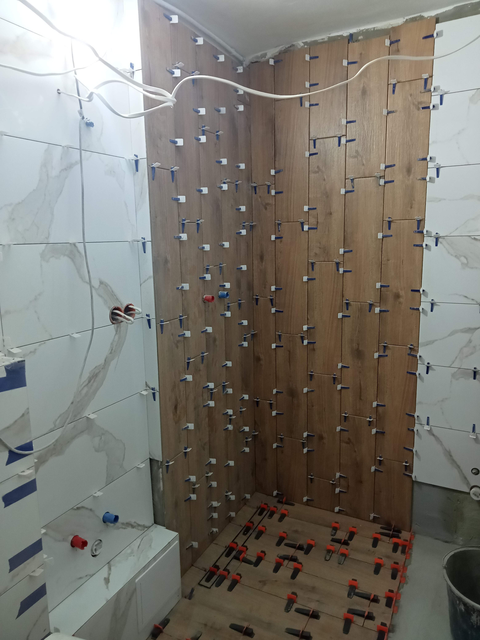Montaż płytek imitujących drewno w łazience w Krakowie, z użyciem systemu poziomowania płytek, widoczne fragmenty instalacji wodnej i elektrycznej.
