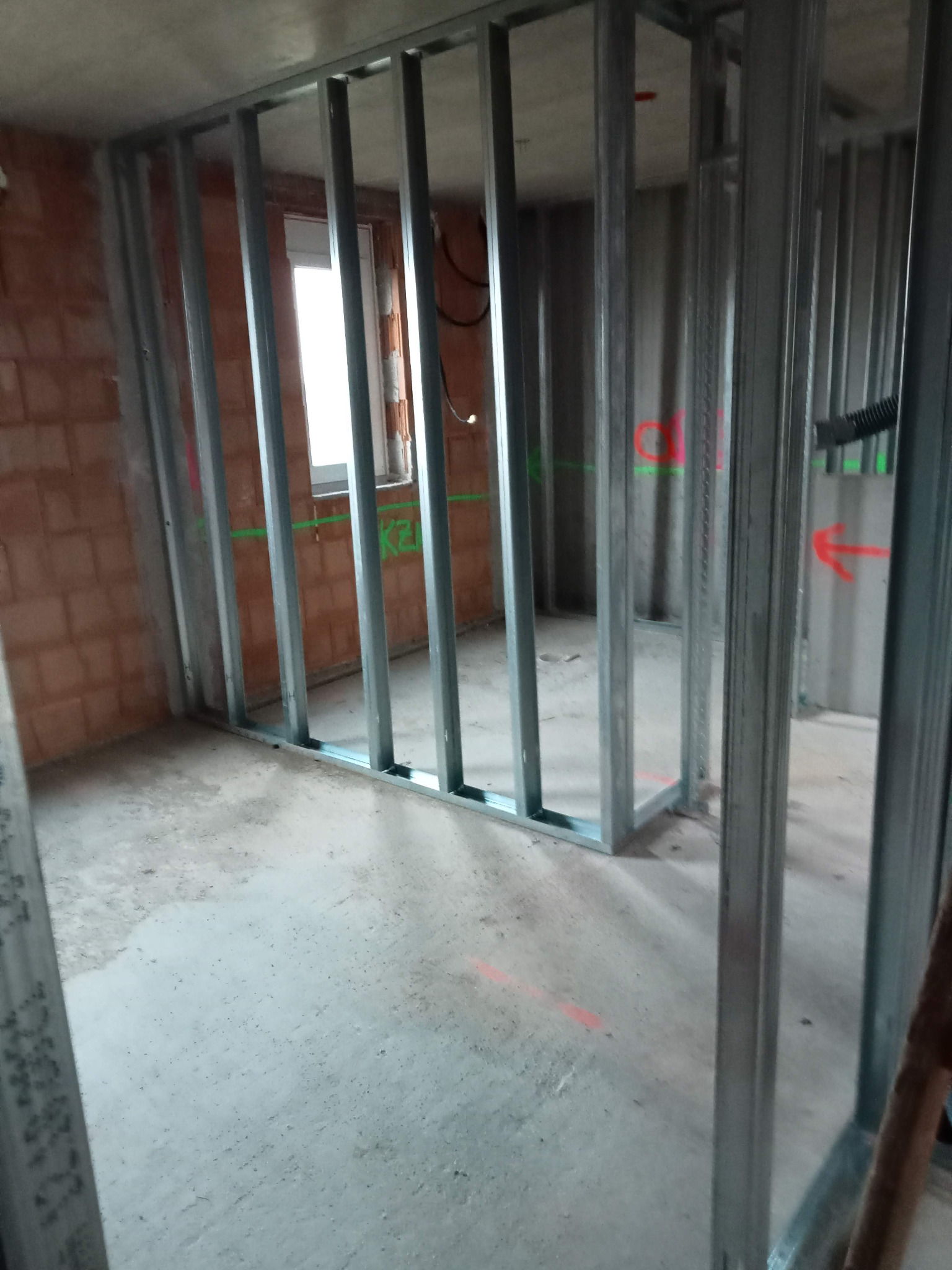 Stelaż z profili metalowych przygotowany do montażu płyt gipsowo-kartonowych, widoczne ślady po oznaczeniach laserowych na ścianach i podłodze, w tle okno.