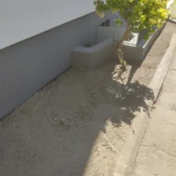 Ocieplona elewacja budynku z widocznym fragmentem fundamentu i posadzoną rośliną obok okna piwnicznego.