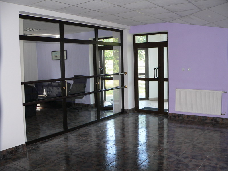 Wnętrze biurowe z przeszkloną ścianą, widoczne biurko z krzesłem, podłoga wyłożona ciemnymi płytkami, ściana pomalowana na fioletowo, biały grzejnik