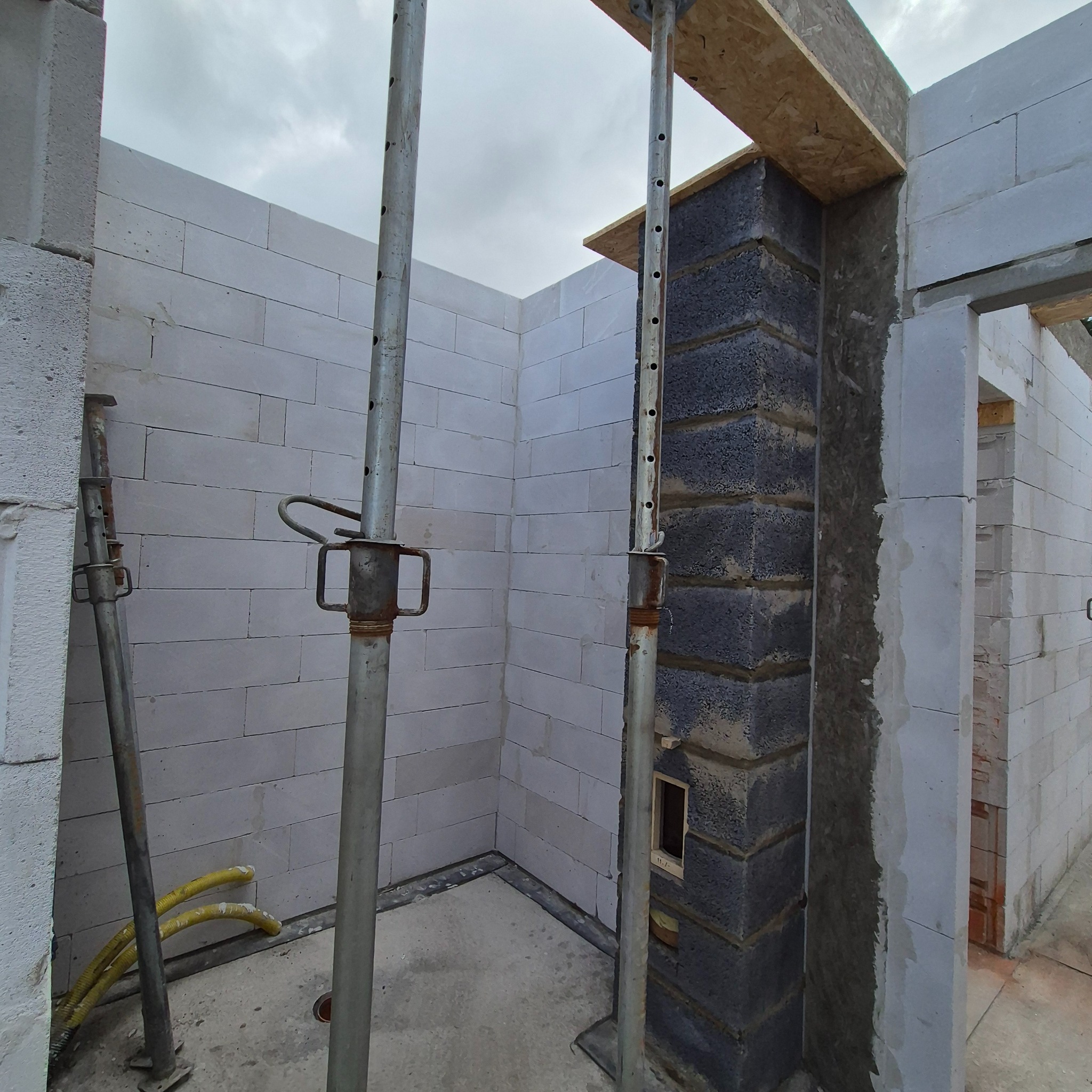 Wnętrze w trakcie budowy: ściany z białych bloczków, szare bloczki narożne, stemple budowlane podtrzymujące nadproże, widoczne instalacje elektryczne.