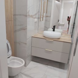 Zakład Ogólnobudowlany - Nowoczesna łazienka z wiszącą toaletą, umywalką nablatową na szafce z drewnianym blatem i marmurowymi płytkami na ścianach oraz podłodze, oświetlona wiszącymi złotymi lampami.