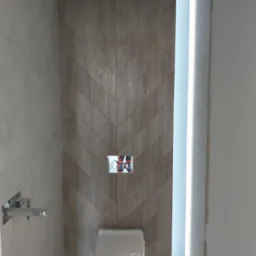 Nowoczesna łazienka z toaletą podwieszaną, drewnopodobne płytki ułożone w jodełkę na ścianie, chromowana bateria umywalkowa i podświetlenie LED w niszy.