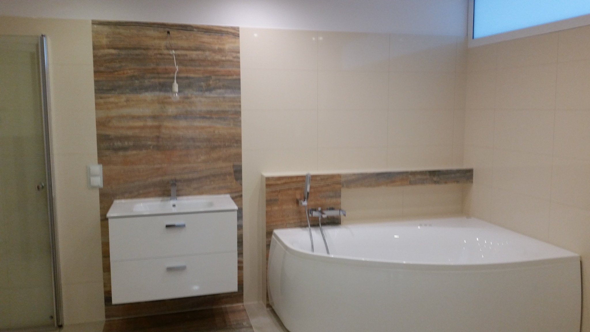 Nowoczesna łazienka z narożną wanną, białą szafką pod umywalkę i płytkami imitującymi drewno na ścianie, widok z perspektywy podłogi.