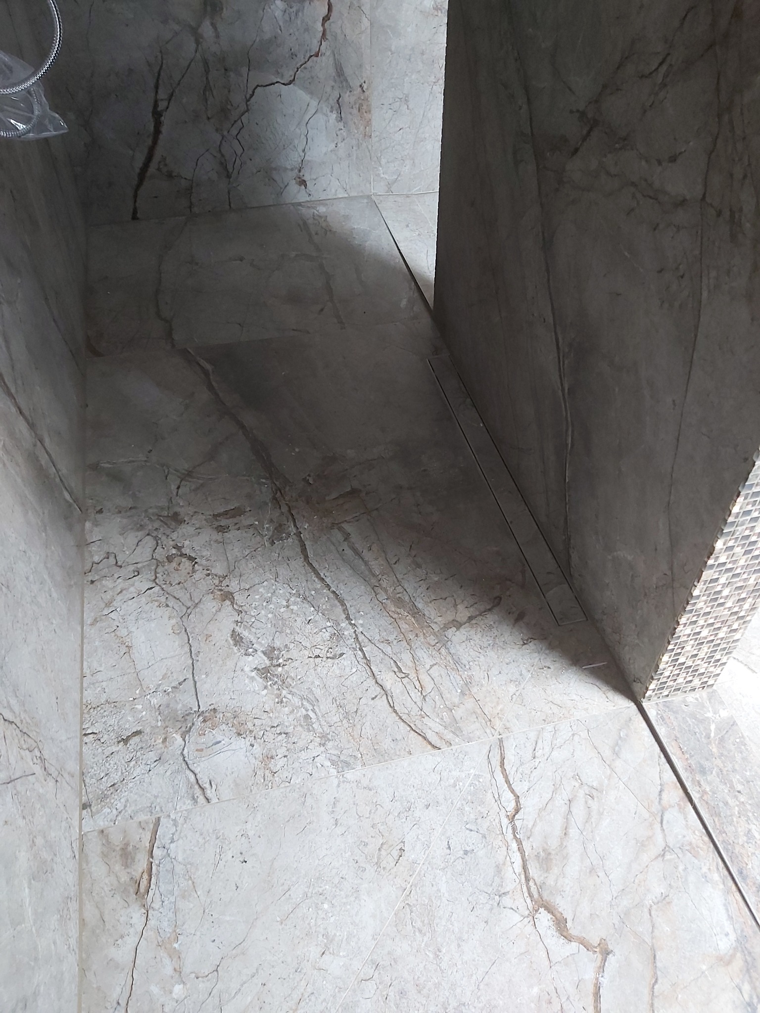 Wykończona kabina prysznicowa z odpływem liniowym w podłodze, wyłożona marmurkowymi płytkami w odcieniach szarości i beżu, widok z góry.