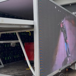 MOKO GROUP SPÓŁKA Z OGRANICZONĄ ODPOWIEDZIALNOŚCIĄ - Mobilny ekran LED na przyczepie prezentujący dynamiczny obraz. Widoczne moduły LED i konstrukcja wsporcza. Detal: czerwony agregat prądotwórczy.