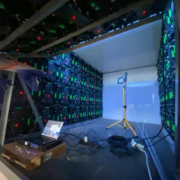 Instalacja modułowej ściany LED z widocznym laptopem i okablowaniem wewnątrz metalowej konstrukcji. Widoczne elementy oświetlenia roboczego i fragment magazynu.