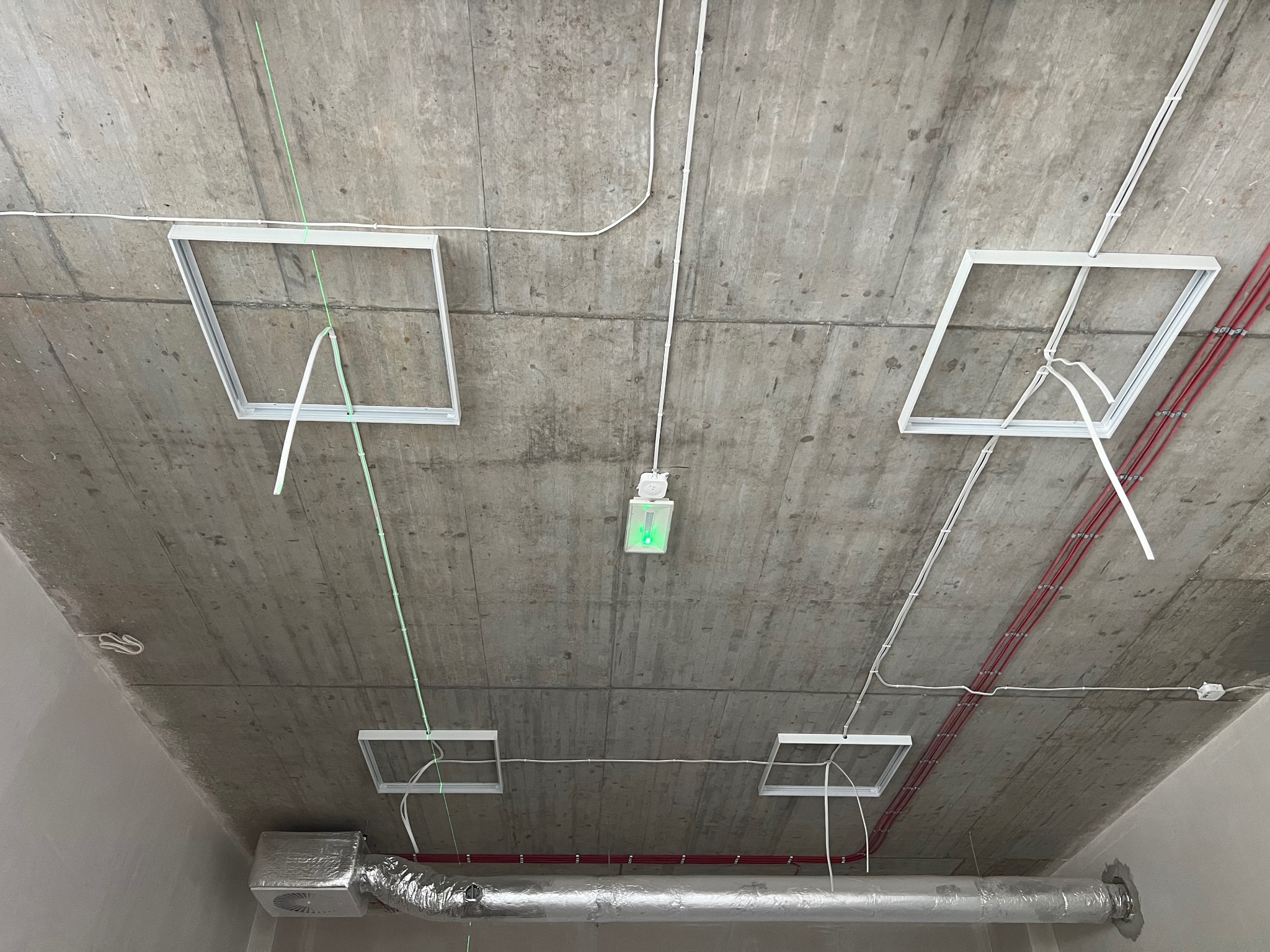 Betonowy strop z instalacją elektryczną w trakcie montażu: widoczne kable w peszlach, puszki instalacyjne i ramy pod oprawy oświetleniowe oraz kanał wentylacyjny.