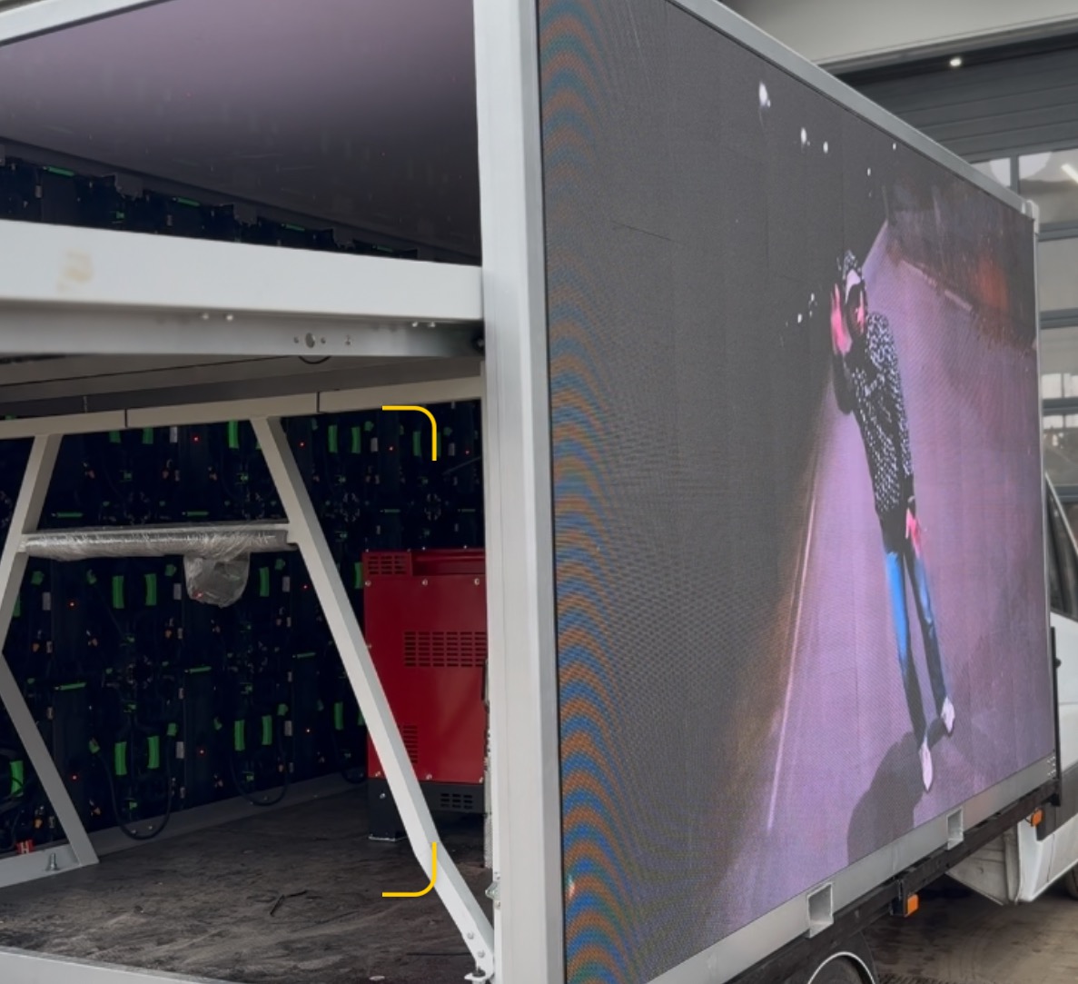 Mobilny ekran LED na przyczepie prezentujący dynamiczny obraz. Widoczne moduły LED i konstrukcja wsporcza. Detal: czerwony agregat prądotwórczy.