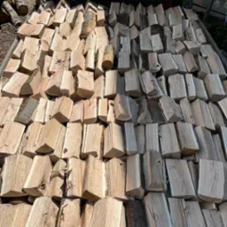 Równomiernie ułożone, pocięte drewno kominkowe w przyczepie z czerwonymi elementami, widoczne słoje drewna i fragmenty kory.