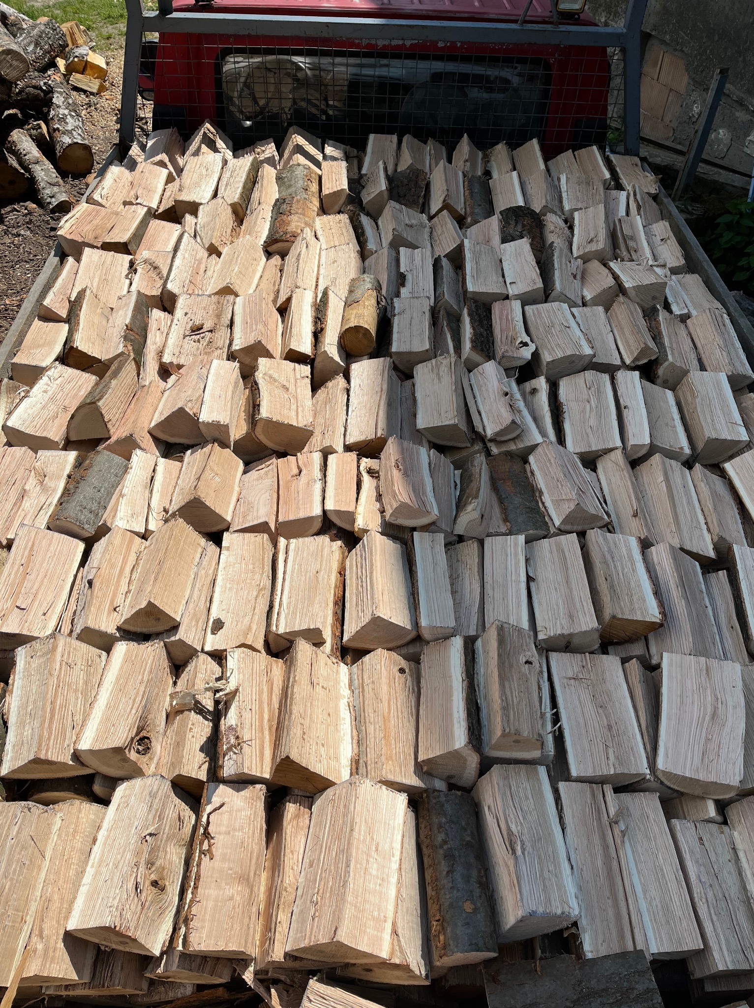 Równomiernie ułożone, pocięte drewno kominkowe w przyczepie z czerwonymi elementami, widoczne słoje drewna i fragmenty kory.