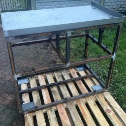 SaldaTech - Stół roboczy ze stali nierdzewnej w trakcie budowy, umieszczony na drewnianej palecie, z widocznym ogrodzeniem betonowym w tle.