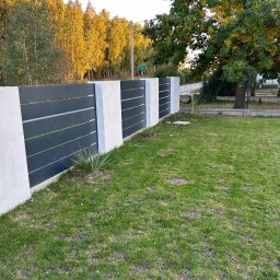 SaldaTech - Nowoczesne ogrodzenie z poziomych, grafitowych paneli oddzielonych białymi, betonowymi słupkami na tle zielonego trawnika i jesiennych drzew.
