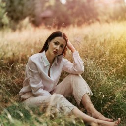 Percepcje Studio Paweł Aleksander Figiel - Portret kobiety siedzącej na trawie w lnianym ubraniu, z ręką opartą o głowę, w naturalnym świetle.