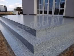 Błyszczące, szare schody zewnętrzne z żywicy epoksydowej prowadzące do domu z dużymi, przeszklonymi drzwiami wejściowymi.